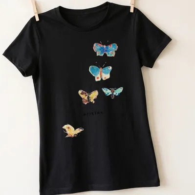 Watercolor print of colorful butterflies surrounding the word 'origins' in elegant script — printed on a women's shirt