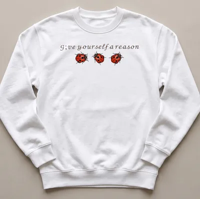 Whimsical ladybug illustration above the text 'G;ve yourself a reason' in red, black, and brown. — printed on a unisex sweatshirt