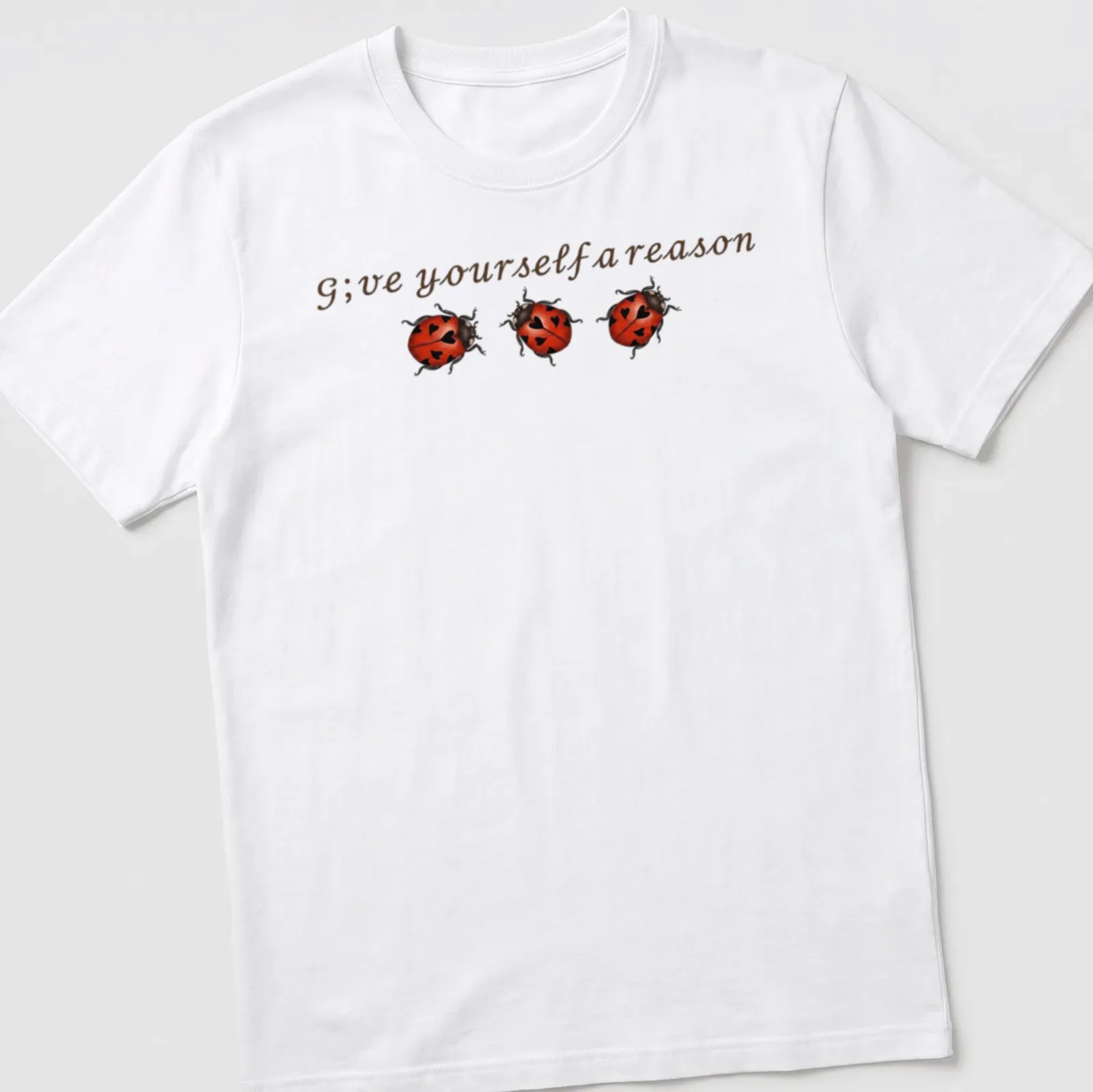 Whimsical ladybug illustration above the text 'G;ve yourself a reason' in red, black, and brown. — printed on a unisex t-shirt
