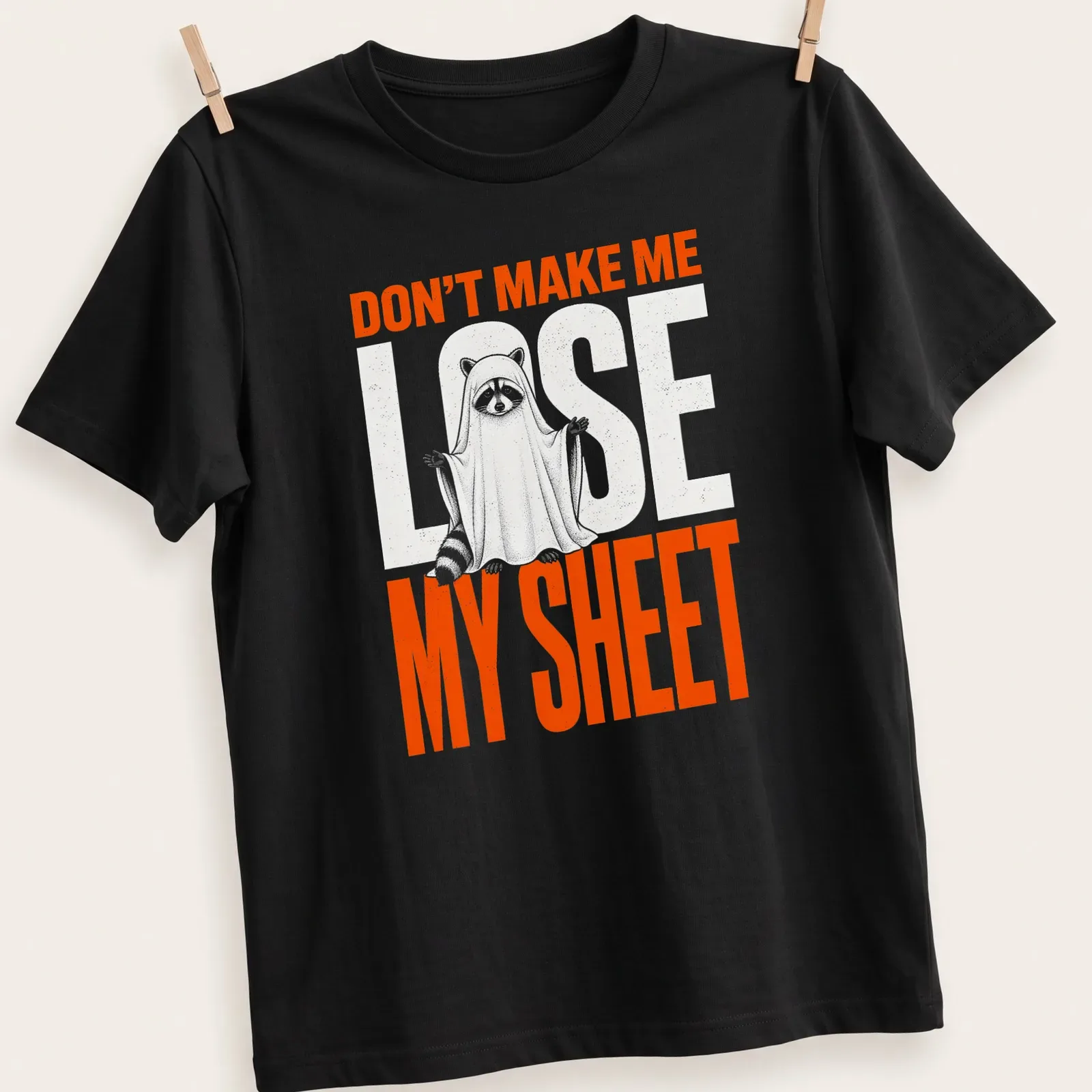 Funny cartoon print of a raccoon ghost with text Don't Make Me Lose My Sheet — printed on a unisex t-shirt