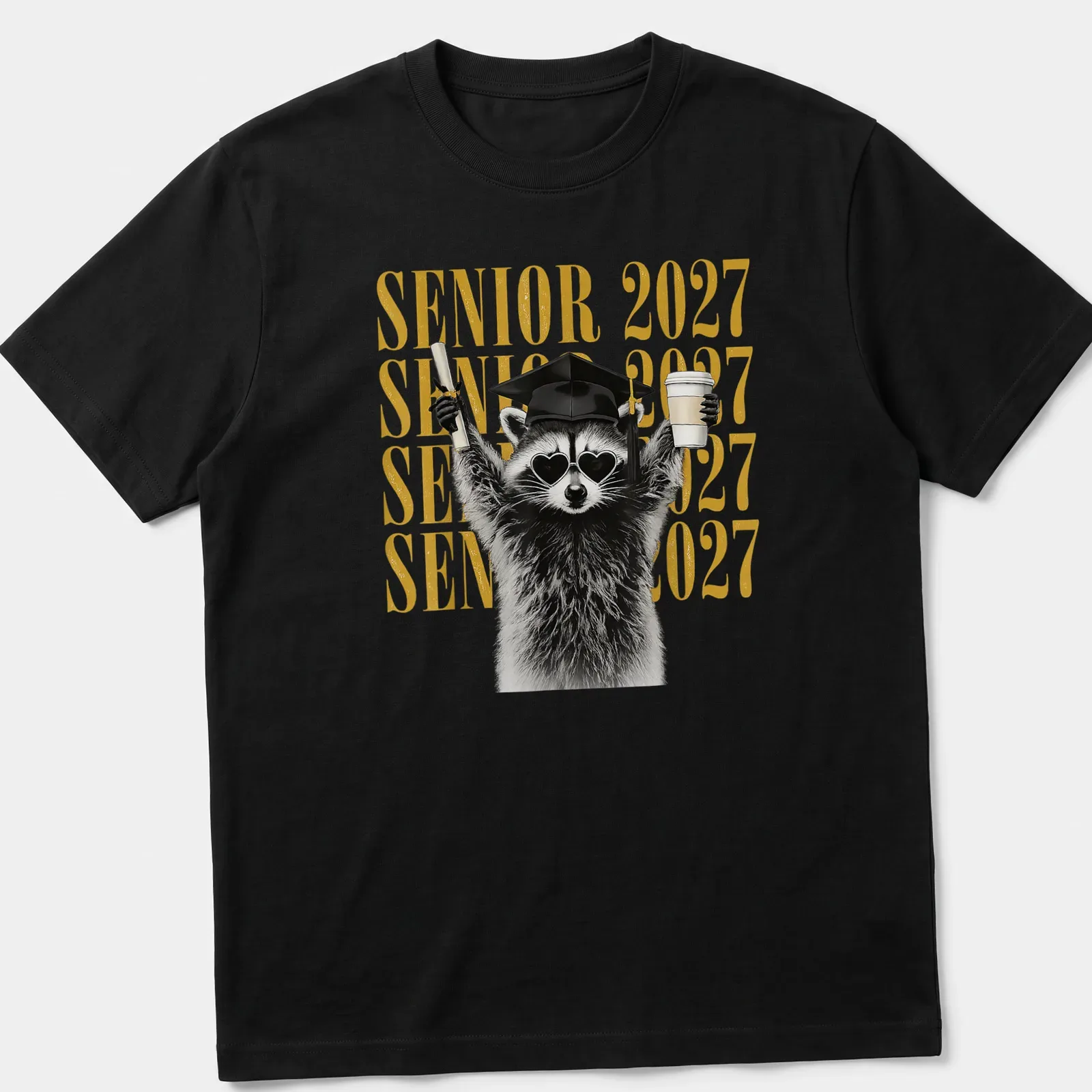 Funny cartoon raccoon with SENIOR 2027 lettering in black, gold, and white — printed on a unisex t-shirt