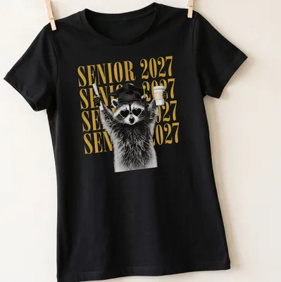 Funny cartoon raccoon with SENIOR 2027 lettering in black, gold, and white — printed on a women's shirt