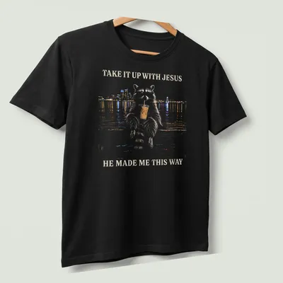 Stylized illustration of a cheeky raccoon with humorous text about Jesus. — printed on a unisex t-shirt (angled view)