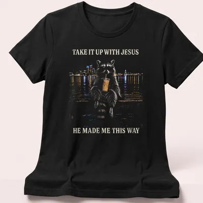 Stylized illustration of a cheeky raccoon with humorous text about Jesus. — printed on a women's shirt
