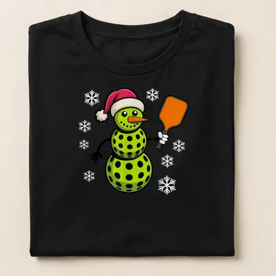 Cartoon snowman playing pickleball in red and green with festive colors — printed on a women's shirt