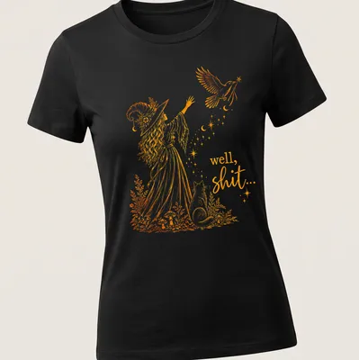 Whimsical illustration of a witch with a crow and magic wand, with text: 'well, shit...' — printed on a women's shirt