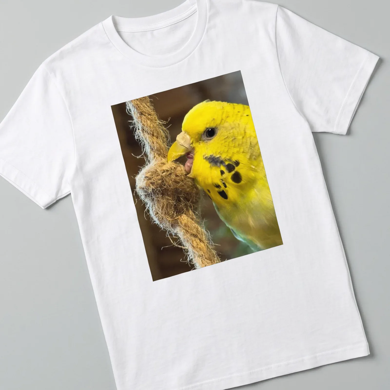 Realistic photograph of a yellow budgerigar perched on a rope against natural colors — printed on a unisex t-shirt